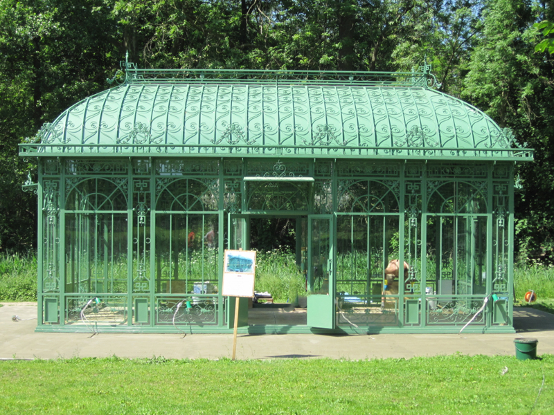 Vintage Victorian greenhouse full exterior view, green ornate metal conservatory in garden lawn