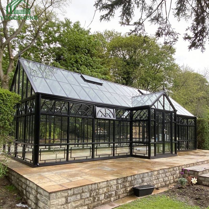 Large black steel Victorian greenhouse set on stone terrace