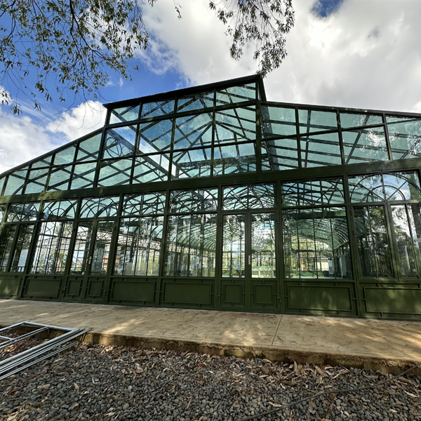 Exterior view of a green-framed glass building with a curved roof against a blue sky.