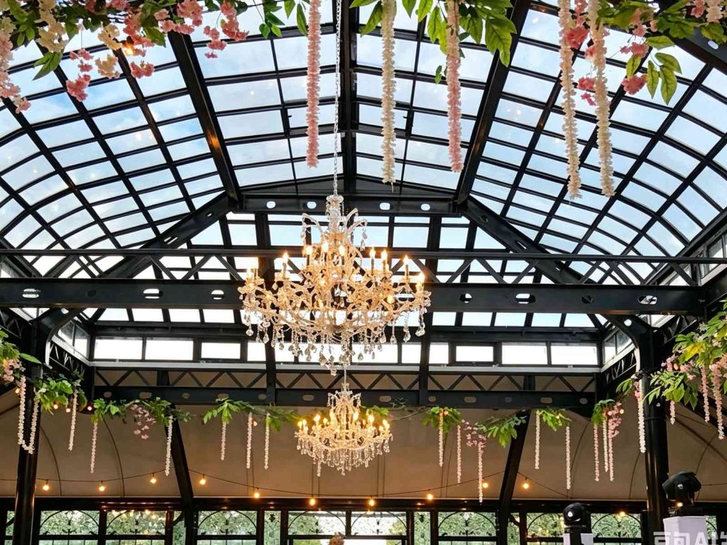 Black metal glass ceiling decorated with pink hanging flower vines and crystal chandeliers for garden wedding venue