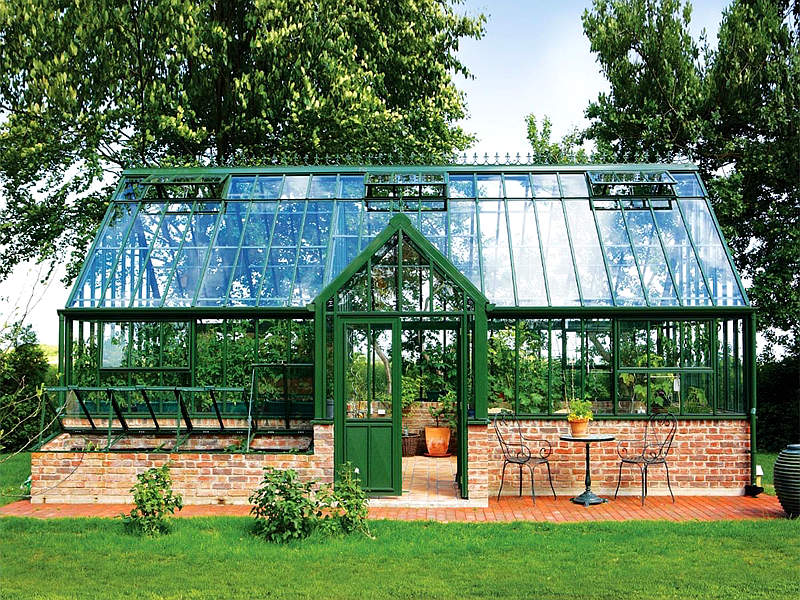 Green painted steel Victorian greenhouse in backyard lawn