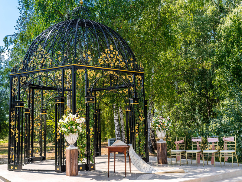 Black gilded vintage wrought iron wedding gazebo set in green woodland for outdoor wedding ceremony