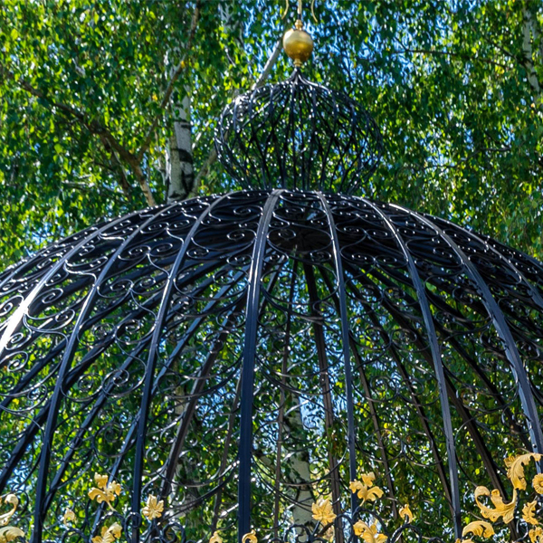 Wrought iron curved dome roof structure of outdoor wedding gazebo amid green trees
