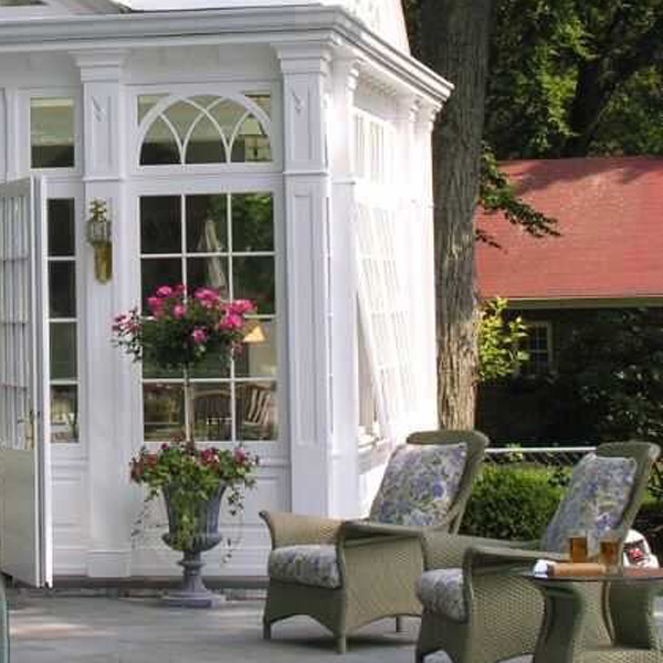 Side facade of white Victorian sunroom beside outdoor garden lounge seating