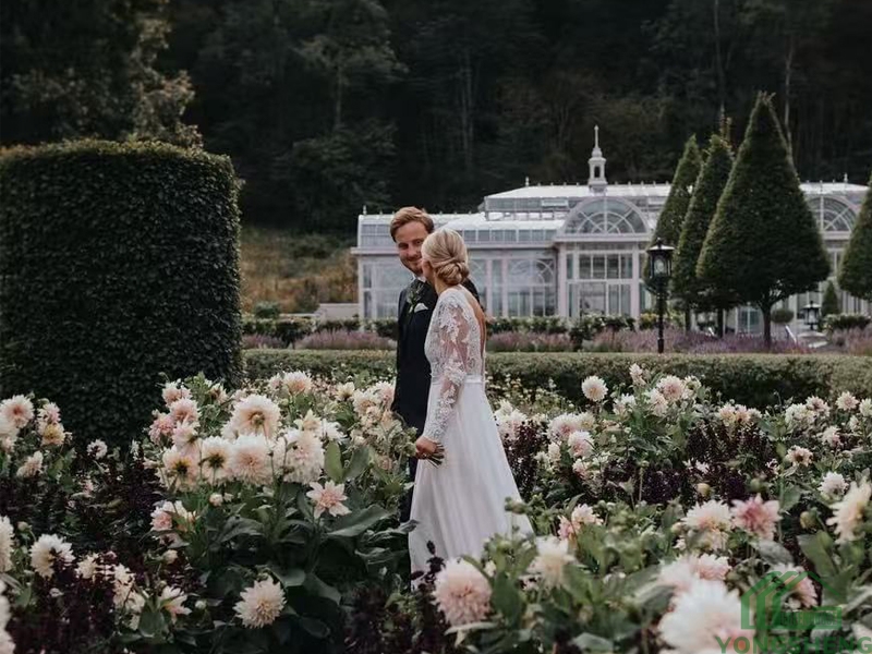 Wedding couple portrait in flower garden with victorian glass conservatory background