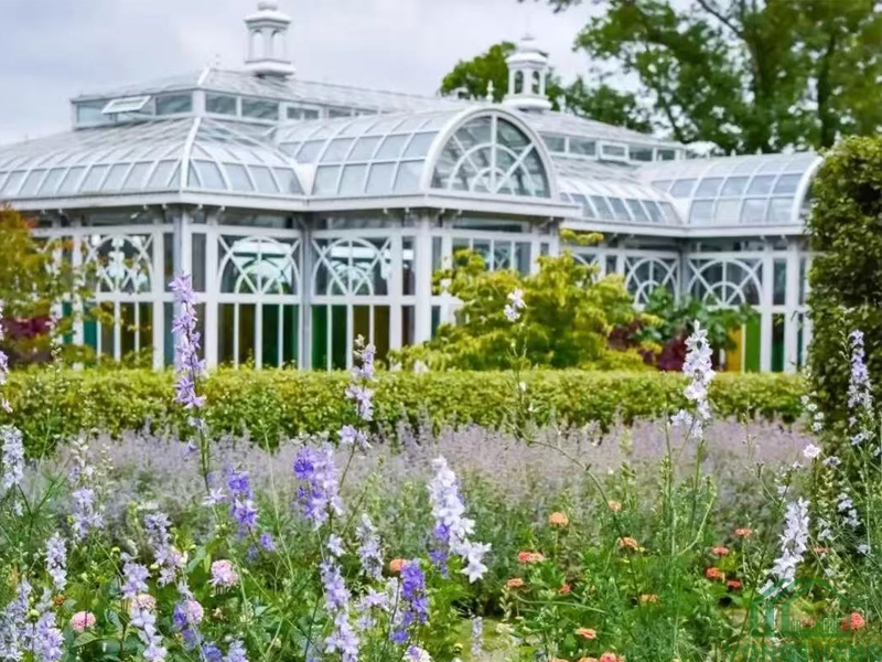 Victorian style glass conservatory surrounded by colorful flower garden