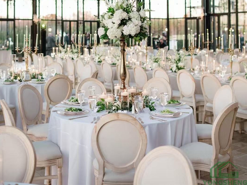 Close-up of a round wedding table with white flowers, candles, and glassware in a greenhouse.