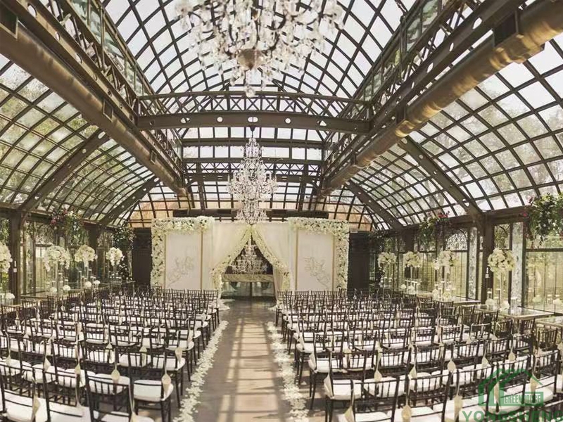 Wedding ceremony aisle with chairs, floral arch, and crystal chandeliers in a glass hall.