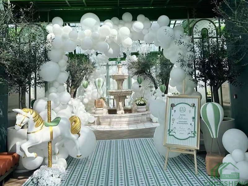 Themed party decoration inside Victorian glass conservatory, white balloon arch, carousel decor, glass greenhouse interior for events