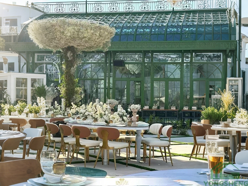 Outdoor wedding banquet tables decorated with white flowers, Victorian green cast iron glass conservatory in background, daytime event venue