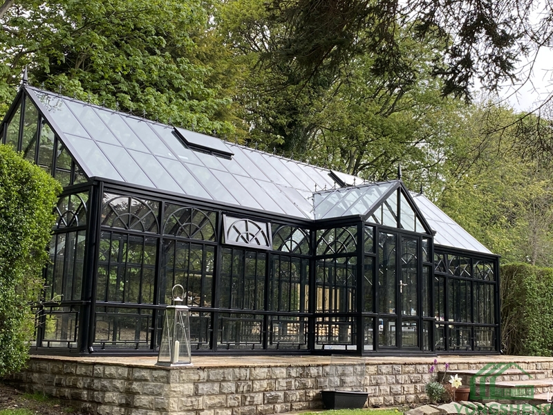 L‑shaped steel frame glass sunroom conservatory on brick base under snowy winter night sky with falling snowflakes