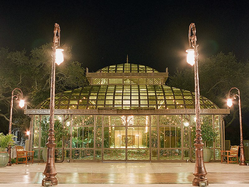 Panoramic night shot of domed steel glass sunroom surrounded by retro ornate street lamps and green trees