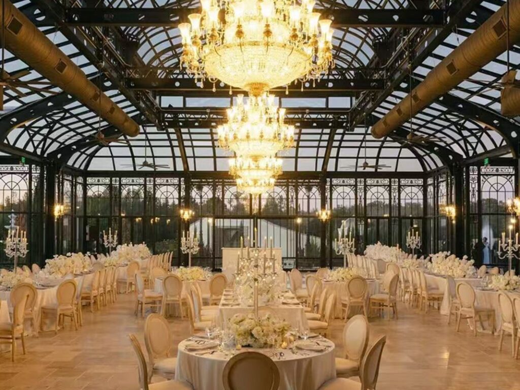 Vintage steel framed sunroom interior furnished with round dining tables for elegant wedding receptions
