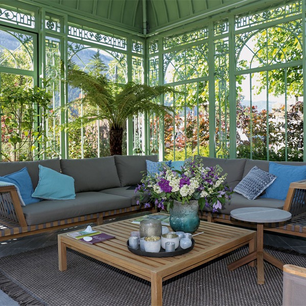 Cozy furnished interior space of victorian green conservatory, lounge sofa set, coffee table and fresh flower decorations