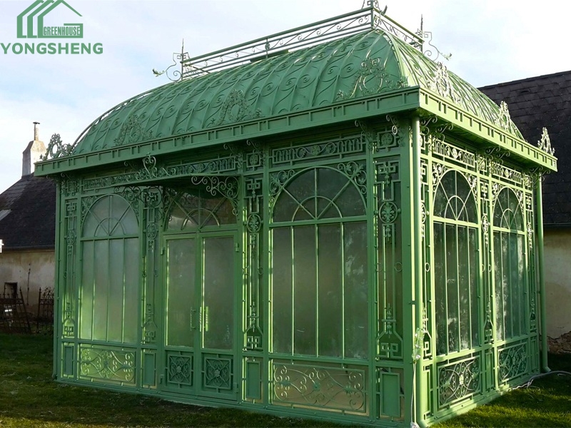 Vintage green galvanized steel Victorian orangery with intricate metal scroll decorations, garden glass pavilion