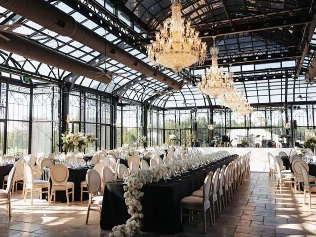 Large glass conservatory with crystal chandeliers and long banquet tables for weddings.