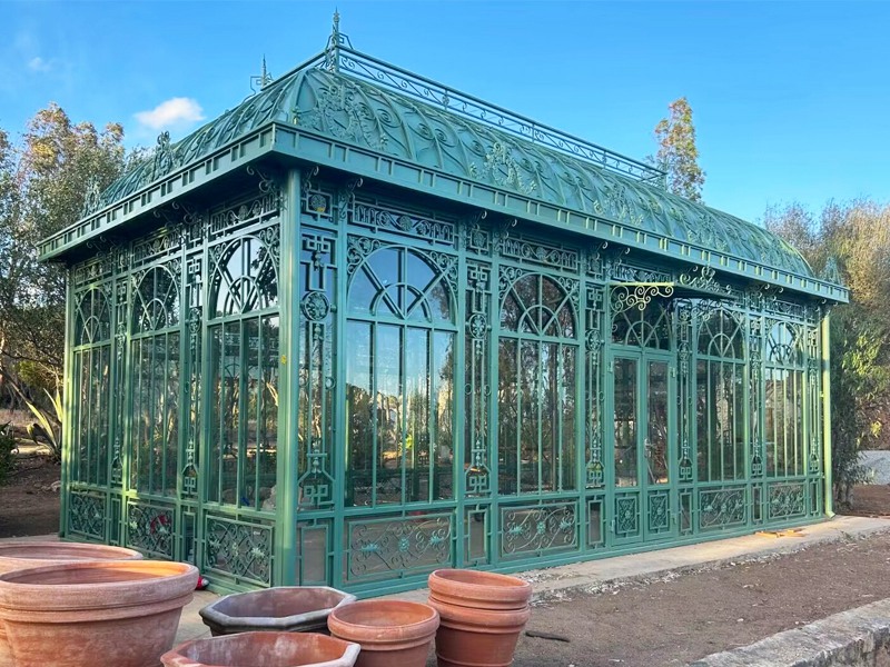 Oversized green steel Victorian conservatory with curved roof and ornate frame patterns for event venue
