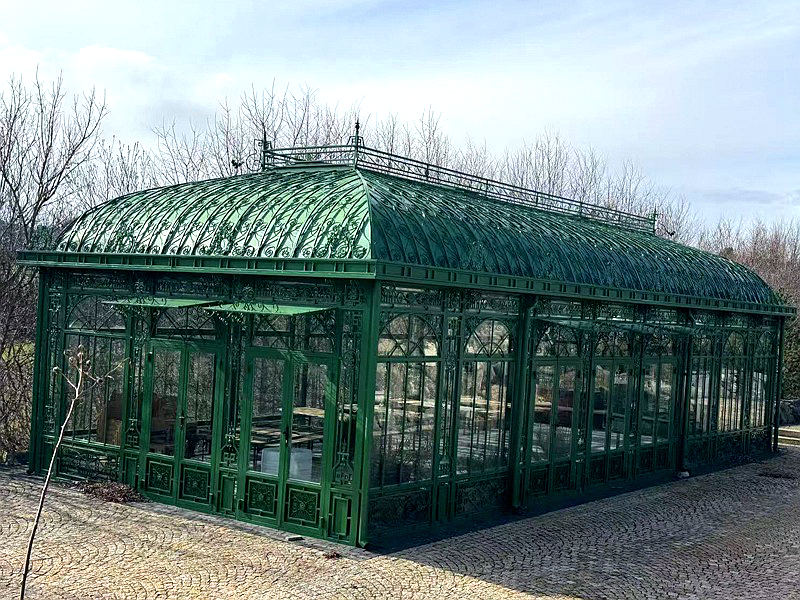 Green curved‑roof Victorian greenhouse YSGH‑057, hot‑dip galvanized steel frame with decorative forged details on paved ground