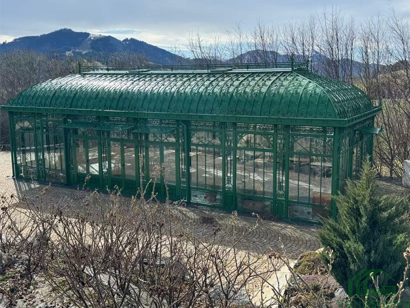 Wide angled shot of YSGH‑057 Victorian greenhouse, large green steel orangerie against mountain and bare‑tree landscape