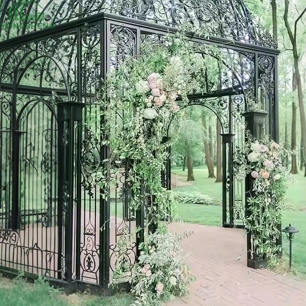 Black metal dome wedding gazebo decorated with fresh flower arch in green garden setting