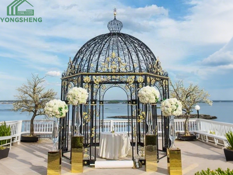 Luxury black metal wedding gazebo with gold decorative accents on waterfront terrace venue