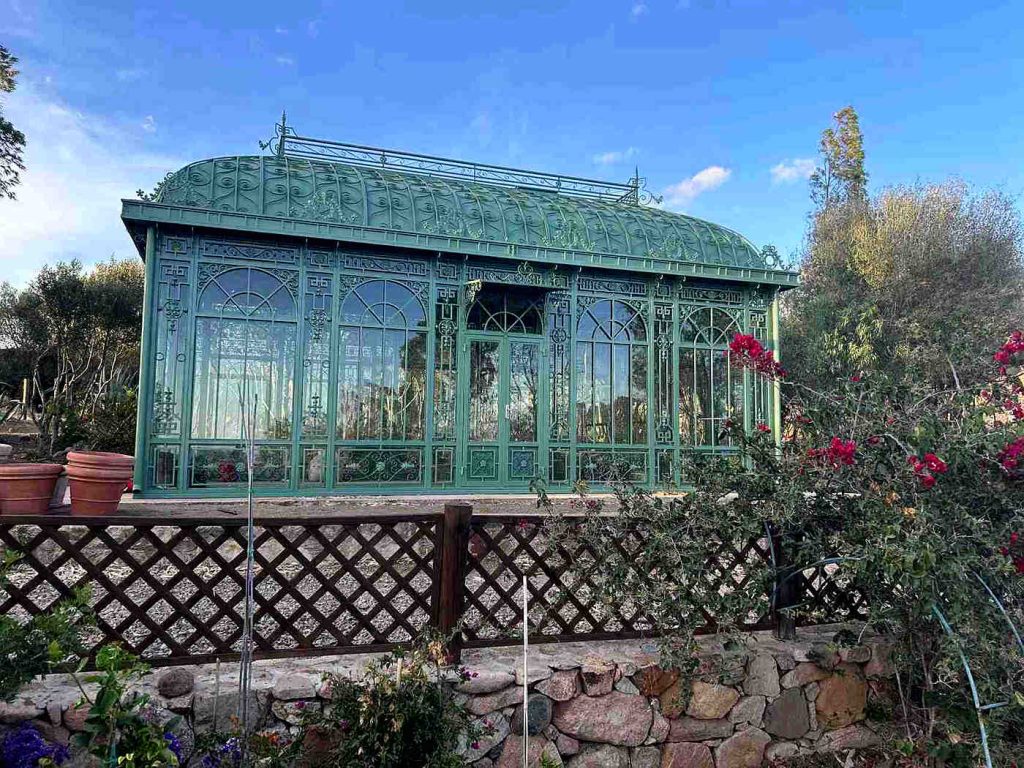 Outdoor Victorian sunroom installed on a stone base with wooden lattice fence and flowering plants