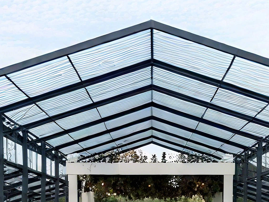 Close-up of black metal A-frame roof structure with clear corrugated PVC panels for an outdoor wedding canopy.