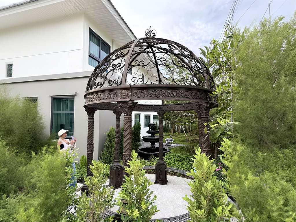Ornate cast iron gazebo placed in residential villa backyard garden