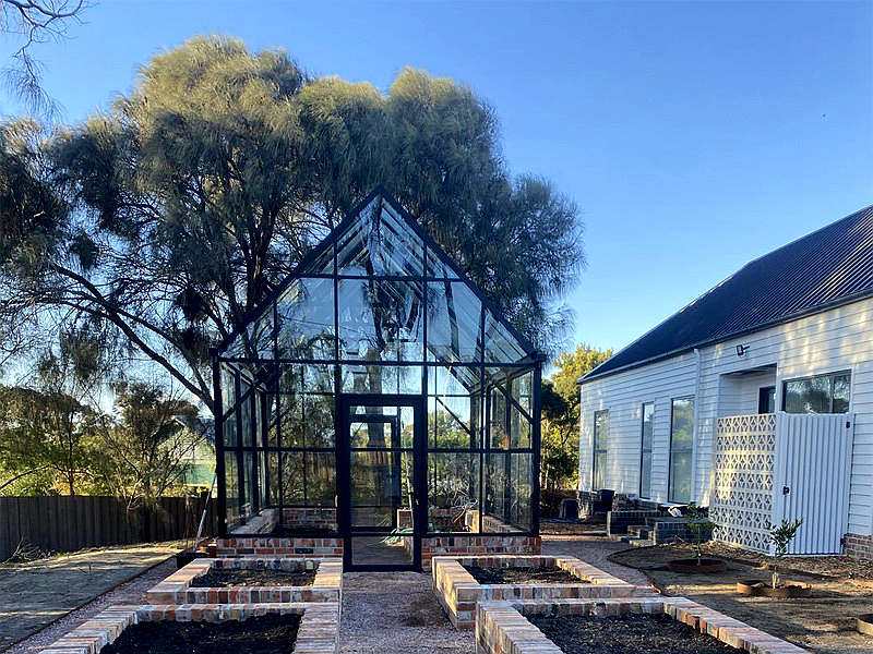 Victorian gable aluminum greenhouse with clear glass panels set in private backyard landscape
