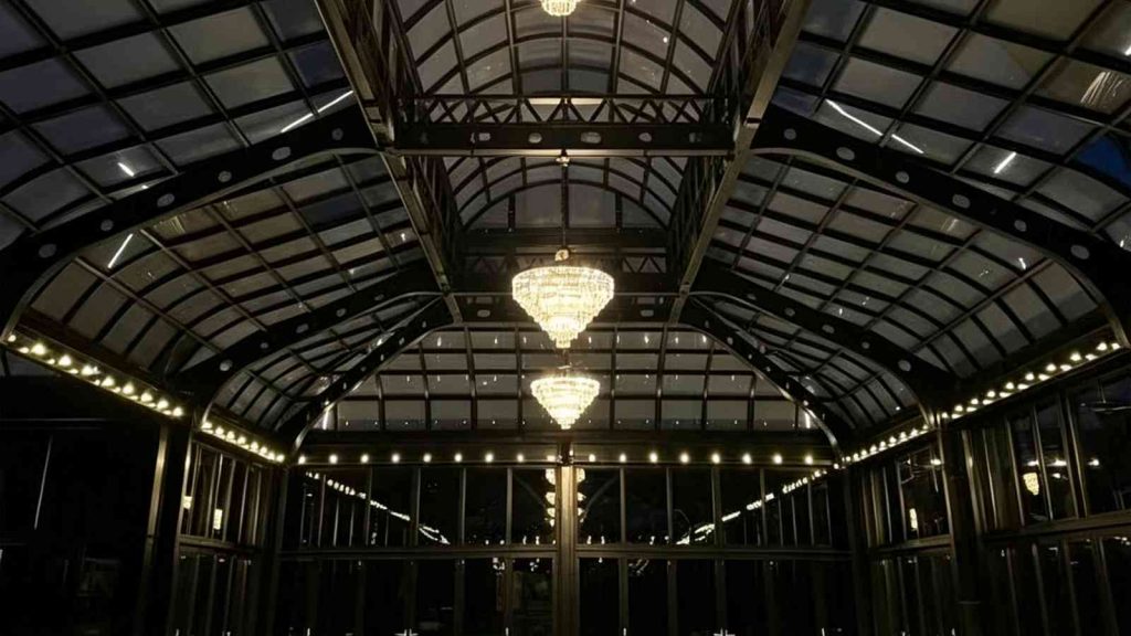 Night interior of Victorian conservatory, steel truss glass roof, crystal chandeliers and ambient perimeter lighting