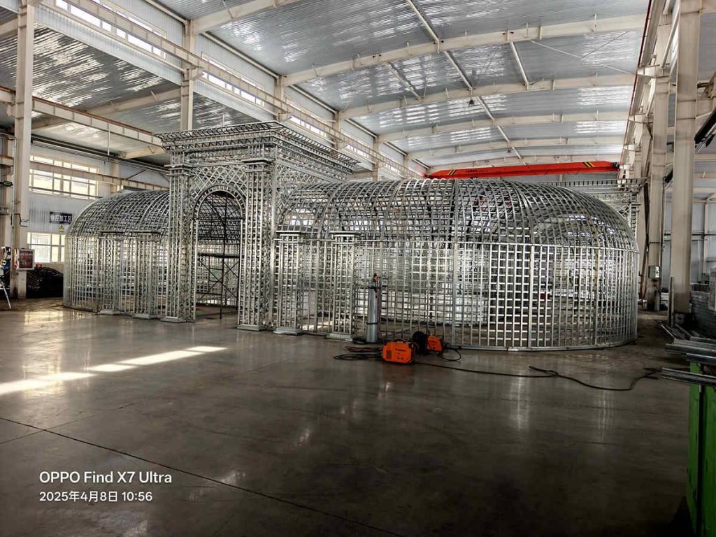 Full‑view factory pre‑assembly of European style steel lattice gateway and arched tunnel pergola, galvanized raw frame inside workshop
