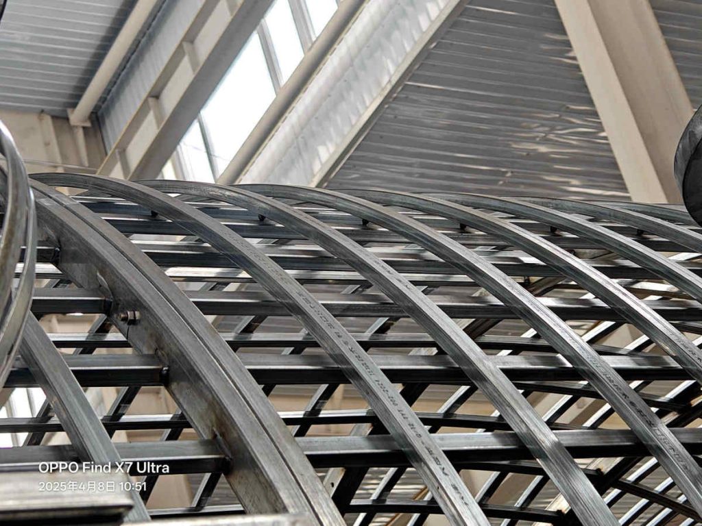 Close‑up detail of curved galvanized steel arched rafter and lattice framework in workshop