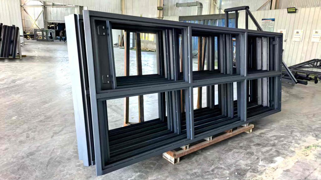 Finished RAL7016 sand grain powder-coated steel window frames stacked on a pallet for the Malta greenhouse.