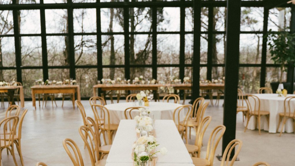 Commercial conservatory glass sunroom interior,banquet table setting with bentwood chairs and floor‑to‑ceiling black steel glass wall