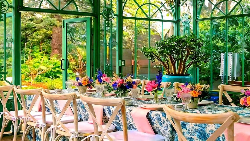 Green frame Victorian greenhouse interior, cozy residential glass sunroom with wicker sofa and tropical plants