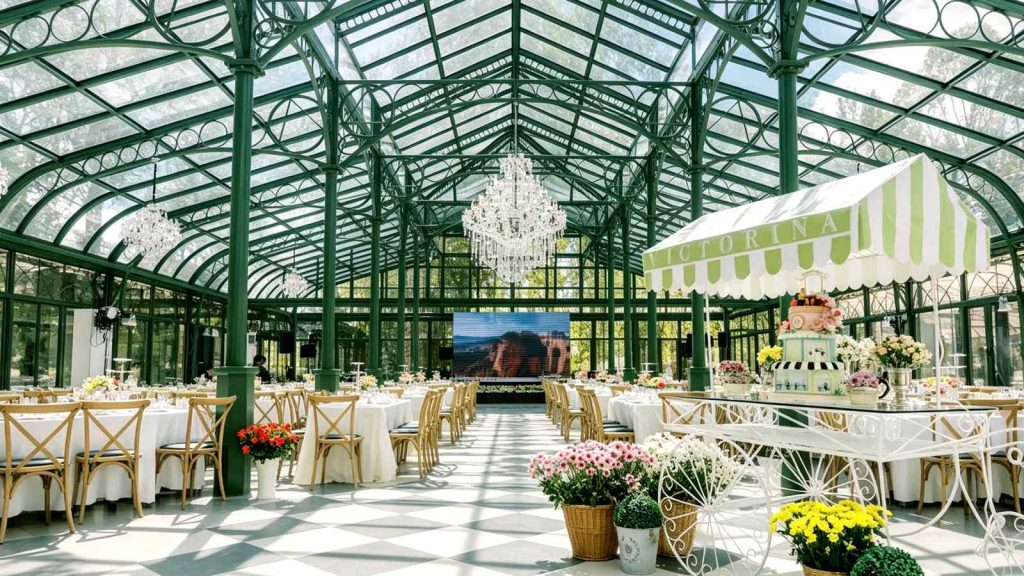 Victorian glass conservatory venue interior with crystal chandelier, dining tables and dessert cart for wedding events